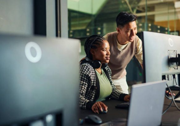 Software engineers collaborating on a project, analyzing code on computer monitors in office